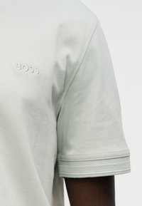 Ανοιχτό γκρι κοντομάνικο t-shirt με κεντημένο λογότυπο «BOSS». διαθέτει υφασμάτινες ριγωτές λεπτομέρειες στα μανίκια. Μαλακό ύφασμα.