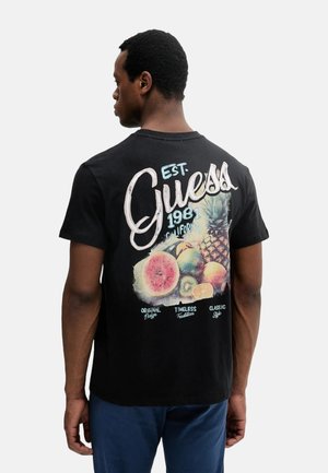 Camiseta de algodón negra con un gráfico colorido de frutas y la palabra "Guess" en cursiva en la parte posterior. Diseño de manga corta y cuello redondo.
