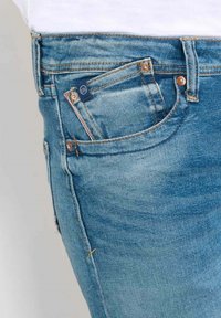 Jeans en denim bleu clair avec un design classique à cinq poches. Présentent des coutures orange, une petite étiquette de logo et une texture décolorée.