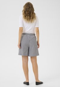 Shorts rayés gris et blanc avec un design plissé et une taille élastique, associés à un haut blanc ajusté et des chaussures noires à enfiler.