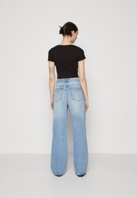 Camiseta negra corta combinada con jeans de mezclilla de pierna ancha en azul claro, con cintura alta y bolsillos traseros, sobre un fondo liso.