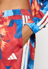 Φλοράλ φόρμα με μοτίβο, σε αποχρώσεις κόκκινου, μπλε και κίτρινου, με λευκές ρίγες και λογότυπο Adidas. Μαλακό, ελαστικό ύφασμα, με ελαστική μέση.