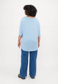 Light blue oversized top with a rounded neckline and three-quarter sleeves, paired with loose blue jeans and sneakers.