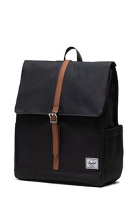Zaino in tela nera con una tracolla e fibbia in pelle marrone, dotato di chiusura a patta, tasca laterale e etichetta con marchio.
