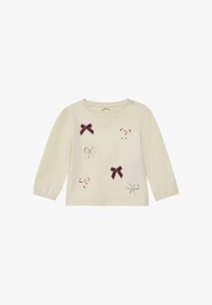 Langärmliges cremefarbenes Baumwolloberteil mit mehreren dekorativen Schleifen in verschiedenen Farben, von denen einige mit Pailletten verziert sind, und Druckknöpfen an den Schultern.