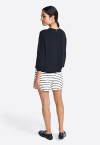 Marineblauwe crewneck trui met driekwartmouwen, gecombineerd met witte shorts met zwarte horizontale strepen en een scalloped rand. Zwarte instappers.
