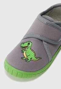 Grå kanvasko med grønn gummisåle, med en brodert grønn dinosaurdesign på toppen. Inkluderer elastiske stropper for enkel påkledning.