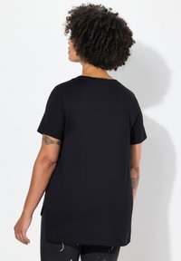 Sort kortærmet t-shirt med en afslappet pasform. Glat tekstur, rund halsudskæring og sideslidser i kanten. Viser tatovering på armen.