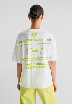 Weißes Baumwoll-T-Shirt mit oversized Passform, kurzen Ärmeln und lebhaftem grünen Grafiktext auf dem Rücken, einschließlich eines Herzens und Koordinaten.