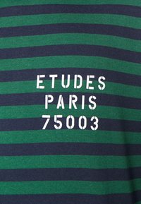 Gestreiftes T-Shirt in Grün und Marineblau mit auffälligem weißen Drucktext: "ETUDES PARIS 75003," im klassischen Rundhalsdesign.