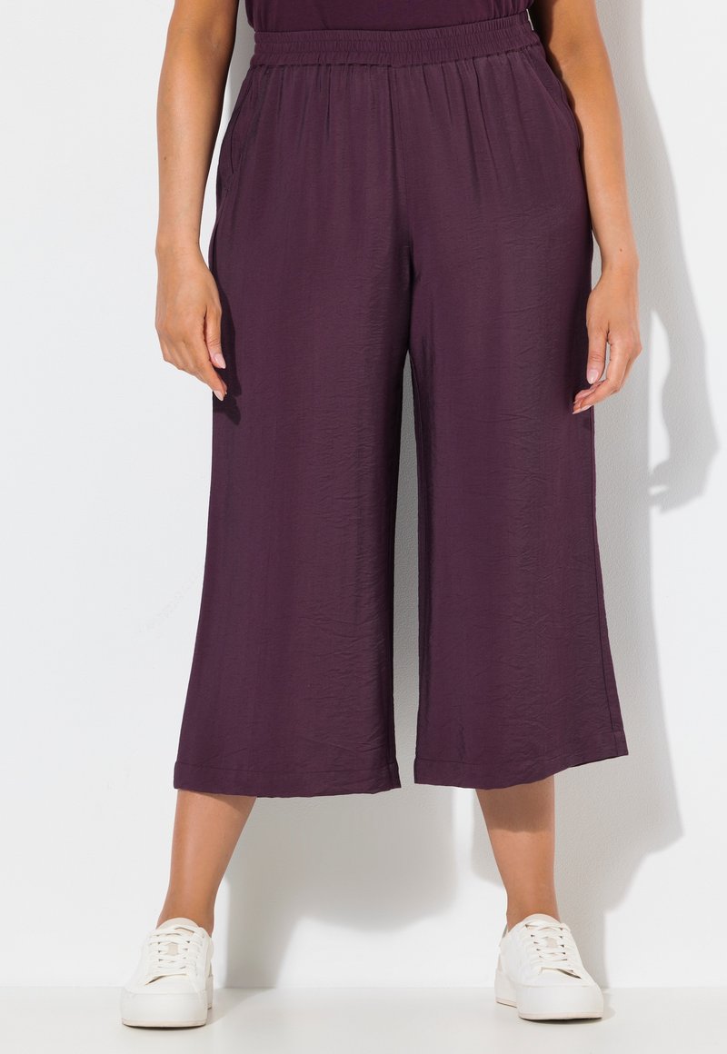 Fialové culottes kalhoty s elastickým pasem, texturovanou tkaninou a širokým střihem, doplněné bílými teniskami.
