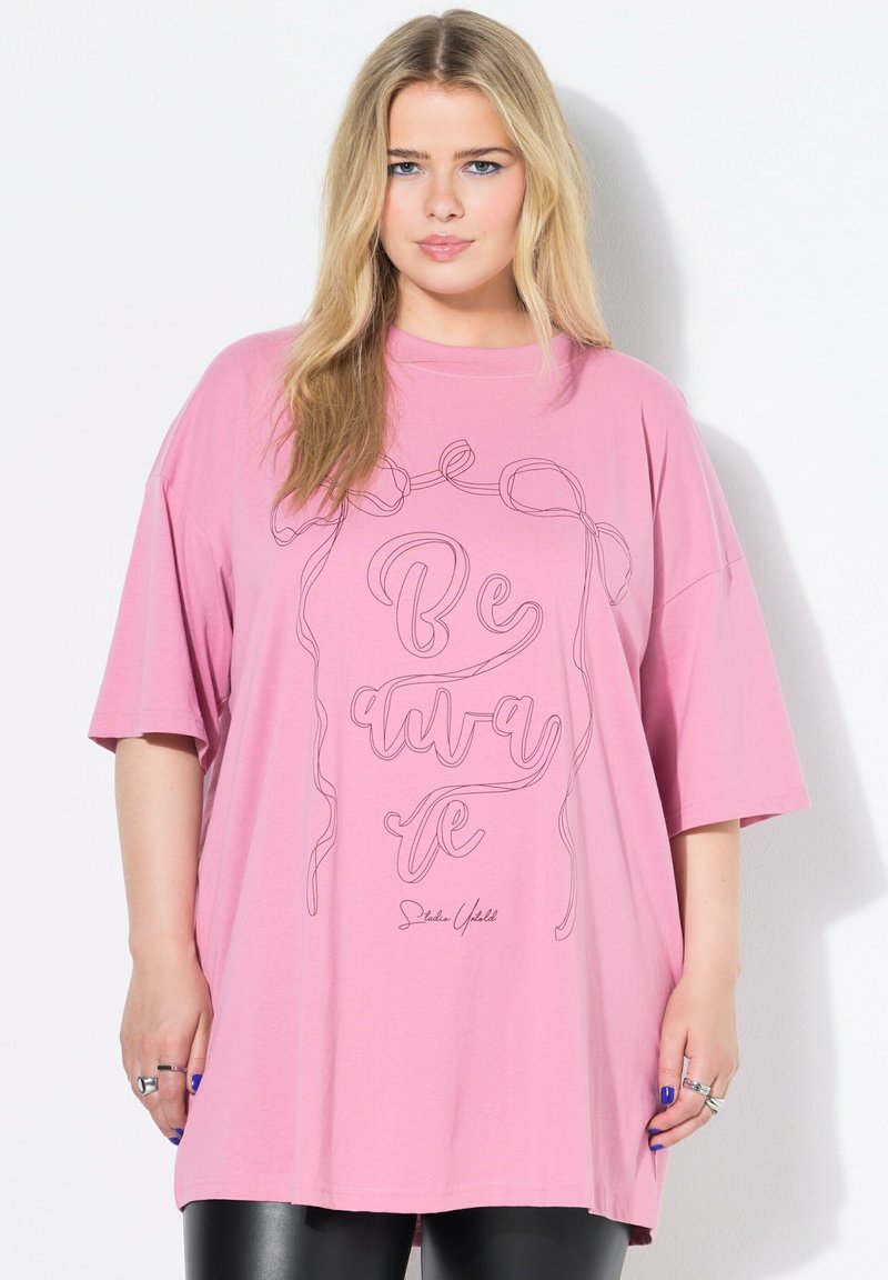 Rosa, oversized T-Shirt mit kurzen Ärmeln, das den Text "Be Aware" in schwarzer Umrandung zeigt, aus weichem Baumwollstoff mit glatter Textur.
