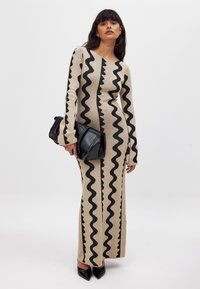 Pikk, kehakujuline beez kleit mustade ziku-idi mustritega, pikad varrukad ja ümmargune kaelus. Kombineeritud musta käekotiga ja teravate kontsadega.