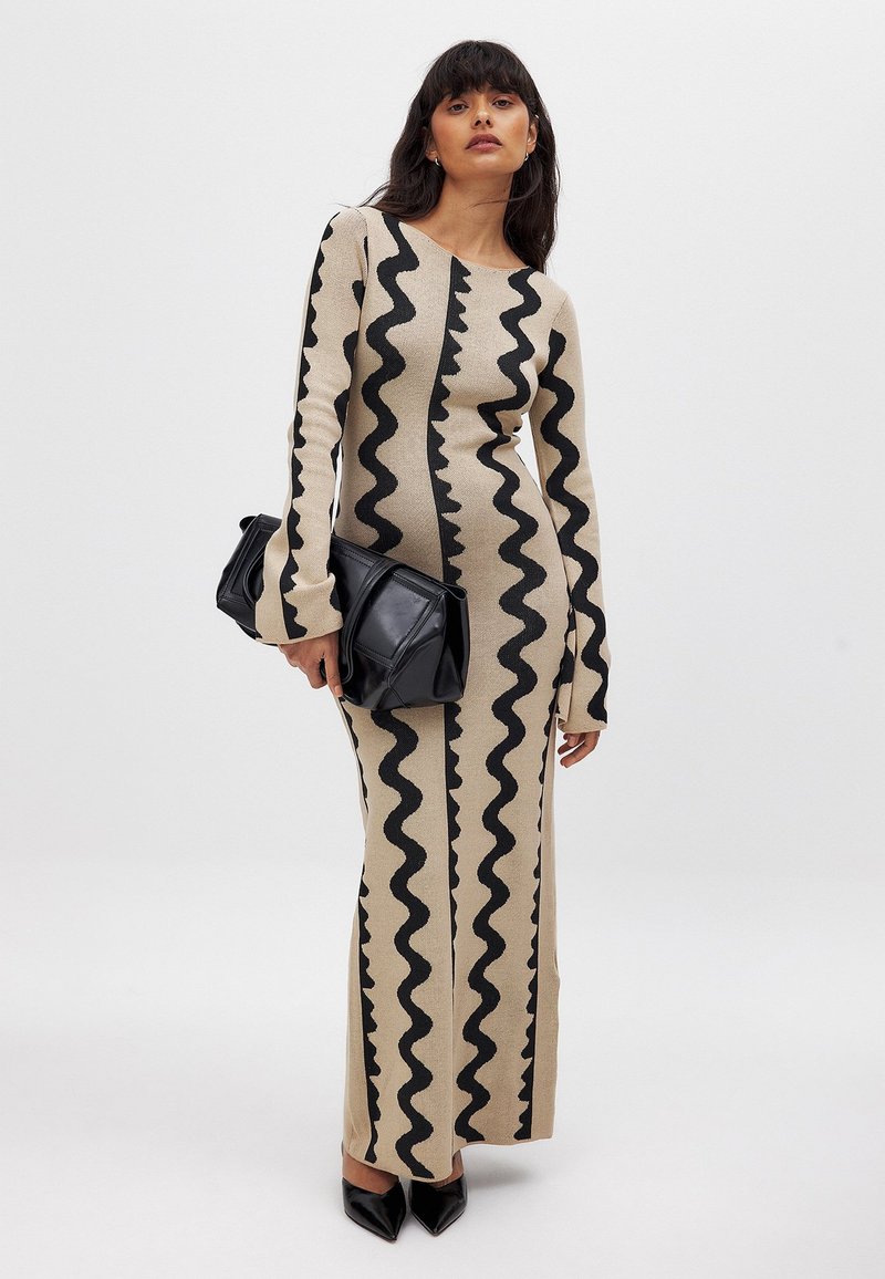 Pikk, kehakujuline beez kleit mustade ziku-idi mustritega, pikad varrukad ja ümmargune kaelus. Kombineeritud musta käekotiga ja teravate kontsadega.