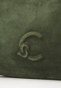 Borsa verde in suede con un design del logo testurizzato e impresso. Superficie liscia con cuciture visibili lungo i bordi.