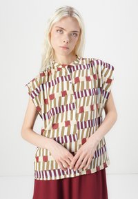 Short-sleeve blouse in a cream background with geometric patterns in burgundy, green, and blue. Rounded neckline with button closure.