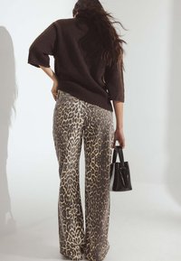 Brūns adīts džemperis un leopardu raksta džinsi ar brīvu piegriezumu. Melna soma rokā, izceļot tekstūras rakstus un malas.