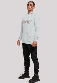 Grå hettegenser med frontlomme, med et flerfarget grafisk design. Svarte cargo-bukser i strukturert stoff, og svarte høye sneakers.