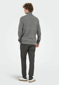 Grijze gebreide trui met hoge kraag, gestructureerde afwerking en lange mouwen, gecombineerd met donkergrijze broek en witte sneakers.