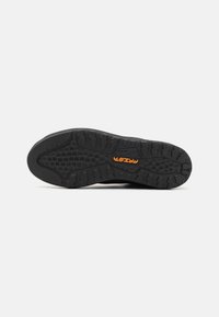Schwarze Außensohle eines Schuhs mit einem strukturierten Grip-Muster, einem hexagonalen Design und einem orangefarbenen Logo mit der Aufschrift "PRISMA" in der Mitte.