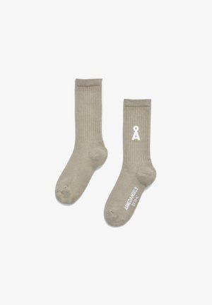 Beige, gerippte Socken aus weichem Material mit einem weißen Logo und Text in der Nähe des Knöchels. Das Design ist einfach und funktional.