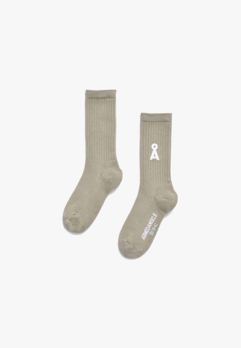 Beige, gerippte Socken aus weichem Material mit einem weißen Logo und Text in der Nähe des Knöchels. Das Design ist einfach und funktional.