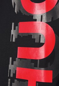 Sort T-shirt med stort grafisk tekstdesign i rød og sølv, med en mat overflade og kontrastrende blanke elementer.