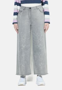 Široké šedé džíny s květinovou výšivkou na přední straně, nezpracovanými lemy a předními kapsami, doplněné o bílé tenisky.