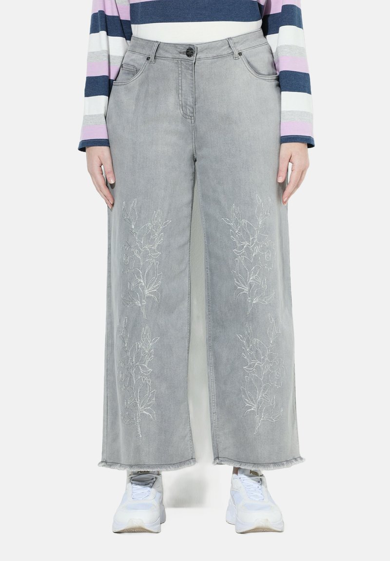 Široké šedé džíny s květinovou výšivkou na přední straně, nezpracovanými lemy a předními kapsami, doplněné o bílé tenisky.