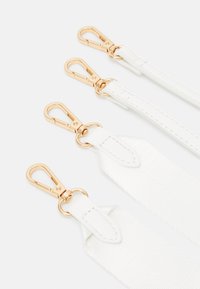 Bretelles blanches avec des clips en métal doré, offrant un tissu texturé lisse et des accents en cuir. Quatre bretelles présentées horizontalement.