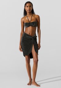 Fekete, bársonyos bikini felsőrész csavart elemmel és vékony pántokkal, hozzáillő redőzött szoknyával, amely magas hasítékkal és csillogó hatással rendelkezik.