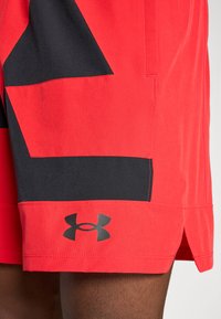 Rode en zwarte Under Armour-shorts met logo op het linkerbeen, gedragen door een persoon met een donkere huid.
