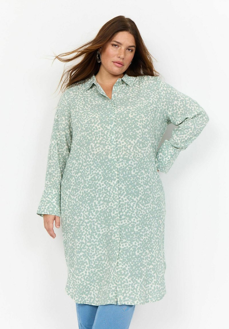 Abito camicia a maniche lunghe di un verde chiaro, con chiusura a bottoni sul davanti, caratterizzato da un motivo astratto bianco a texture. Tessuto morbido con una vestibilità comoda.
