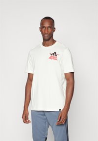 Hvid bomulds T-shirt med et rødt og sort "Adidas Football" logo på venstre bryst. Casual pasform med korte ærmer.