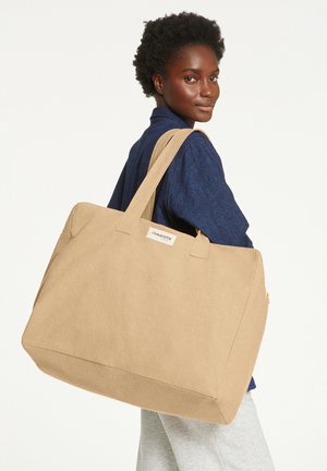 Beige Leinenshopper mit Doppelgriffen, rechteckiger Form und einem Reißverschlussfach. Logosticker auf der Vorderseite, strukturierte Oberfläche.