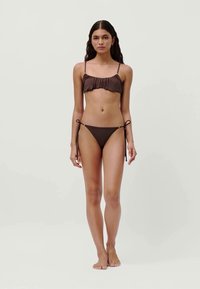 Ensemble de bikini marron comprenant un haut à bretelles volantées et un bas à nouer sur les côtés ajustables, fabriqué dans un tissu lisse au design minimaliste.