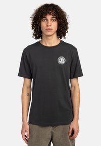 Zwarte katoen t-shirt met korte mouwen, ronde hals en een kleine witte graphic op de linkerkant van de borst. De stof lijkt glad en heeft een ontspannen pasvorm.