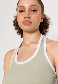 Top halter em verde claro com textura canelada e acabamentos brancos. Design justo com textura suave e estilo costas de nadador.