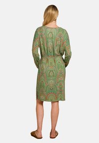 Groene gewatteerde badjas met lange mouwen, met een ceintuur om de taille en zijsplitten. Bevat ingewikkelde bloem- en paisleymotieven.