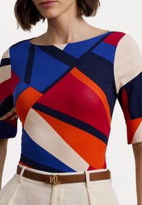 Top multicolor con patrones geométricos en rojo, azul y naranja. Diseño ajustado con mangas cortas. Cinturón marrón con detalles en dorado.
