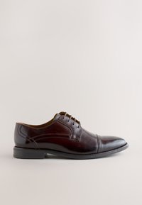 Chaussure habillée homme en cuir marron foncé avec laçage fermé, bout rapporté et talon bas empilé, montrée de profil sur fond neutre.