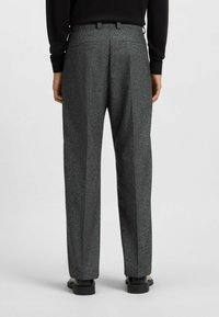 Gray textured trousers with a tailored fit, featuring two back pockets, pleats, and finished hems, worn with black shoes.