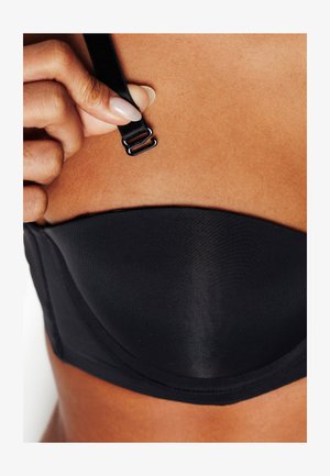Reggiseno imbottito nero caratterizzato da tessuto liscio, spallina regolabile con gancio in metallo e design senza cuciture, mostrato su un tono di pelle.