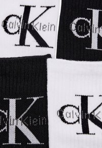 Calze Calvin Klein in bianco e nero. Presentano un logo prominente, una texture a coste e una combinazione di sezioni a tinta unita e a fantasia.