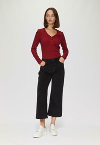 Rode langlopende ribben-top met een knopenpaneel, gecombineerd met zwarte high-waisted wijde broek en witte sneakers.