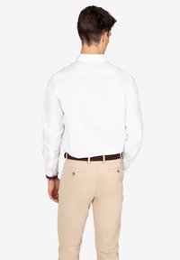 Camisa blanca de manga larga vista desde la parte posterior, con un cuello clásico y detalles de botones. Combinada con pantalones beige y un cinturón marrón.