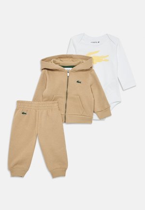 Sweat à zip beige, pantalon assorti et body blanc avec un graphique de crocodile jaune. Matière en coton doux avec des poignets côtelés et des accents de logo.