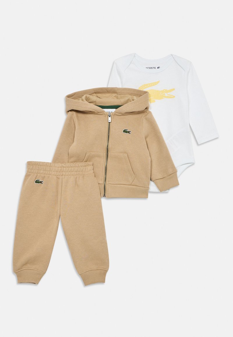 Sweatshirt com fecho éclair na cor bege, calças a condizer e um body branco com gráfico de crocodilo amarelo. Material de algodão suave com punhos canelados e detalhes em logo.