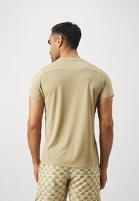Beige kortermet t-skjorte med rund hals, jevn tekstur og subtile skulderdetaljer, sammen med mønstrede beige shorts.