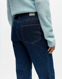 Tamnoplave traperice visokog struka s dva stražnja džepa, kontrastnim šavovima i kožnim logotipom na pojasu.